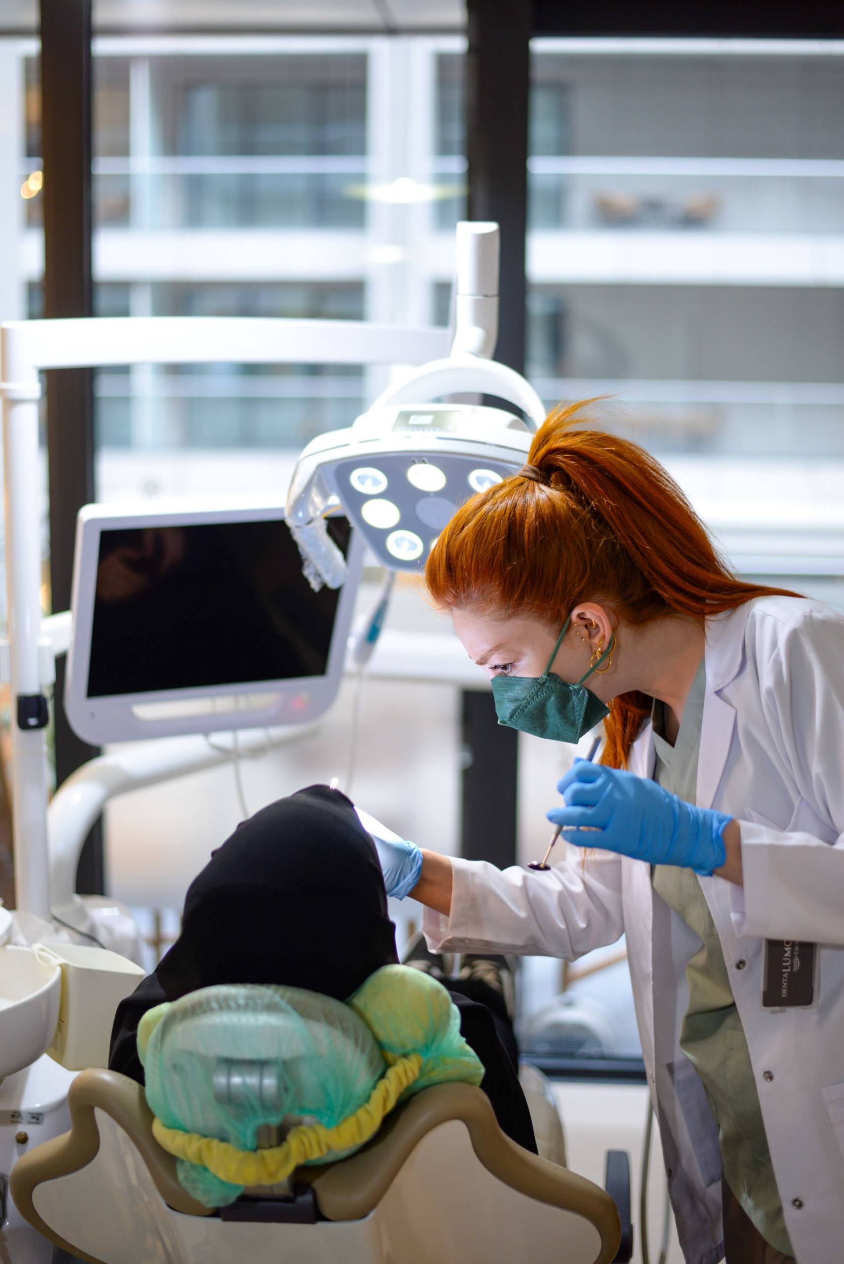 Dentist leaning over a reclined patient during a treatment in a bright, window-lit dental office