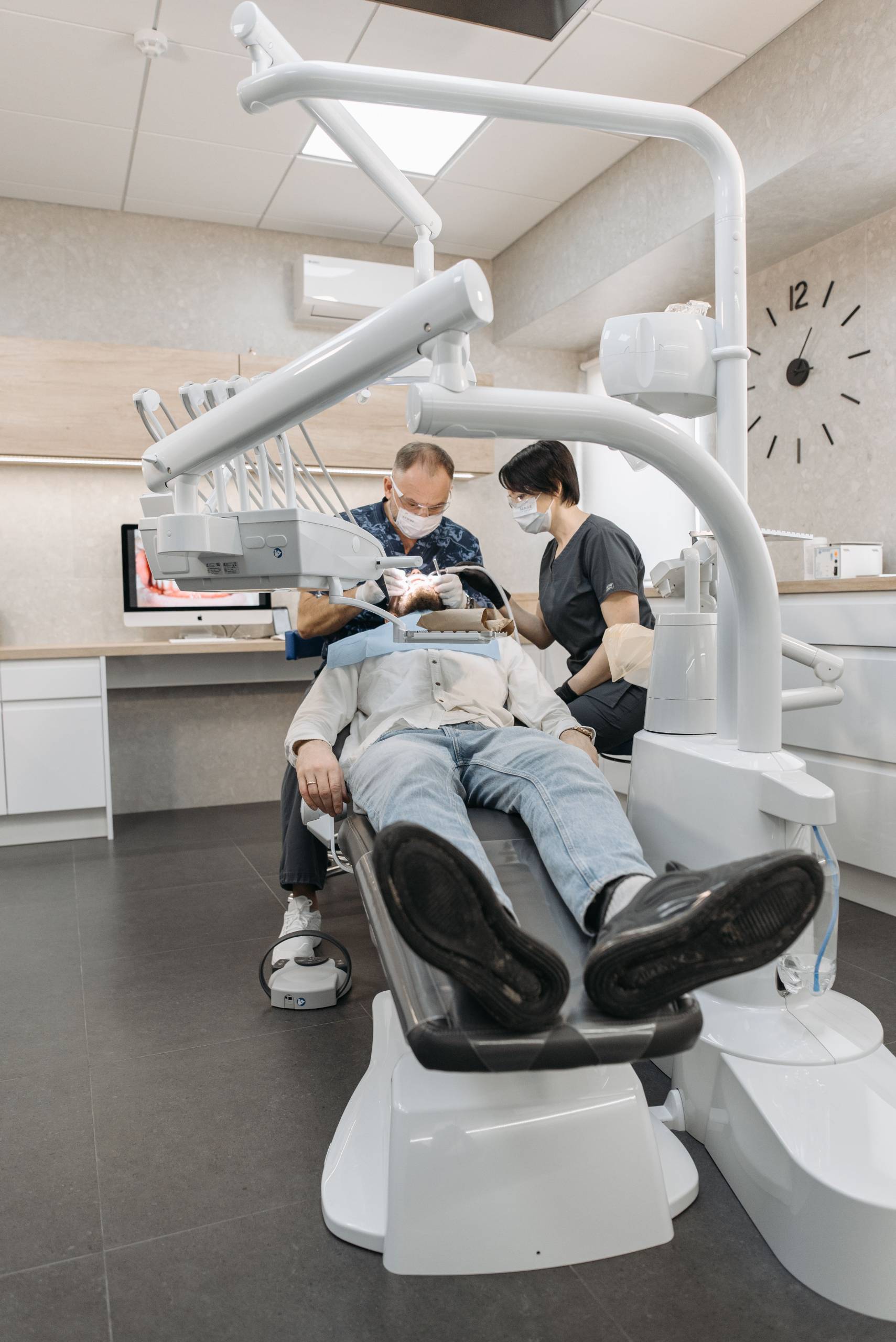Dentist in a white coat examining a patient under the exam light in a bright, contemporary dental office