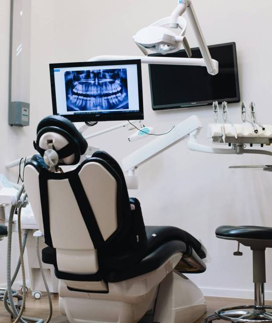 Modern dental exam room with treatment chair, overhead light, and monitor displaying a patient's panoramic dental X-ray